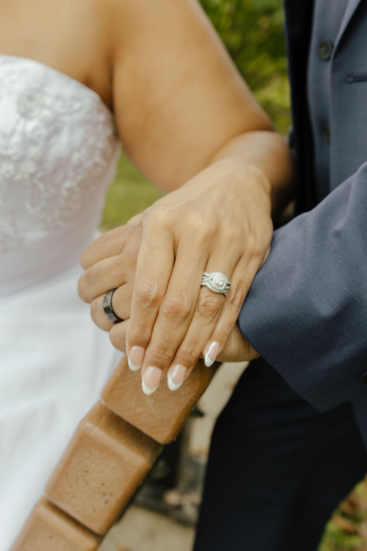 Close-up shot of newlywed couple's hands with wedding rings and formal attire showing in white and gray.