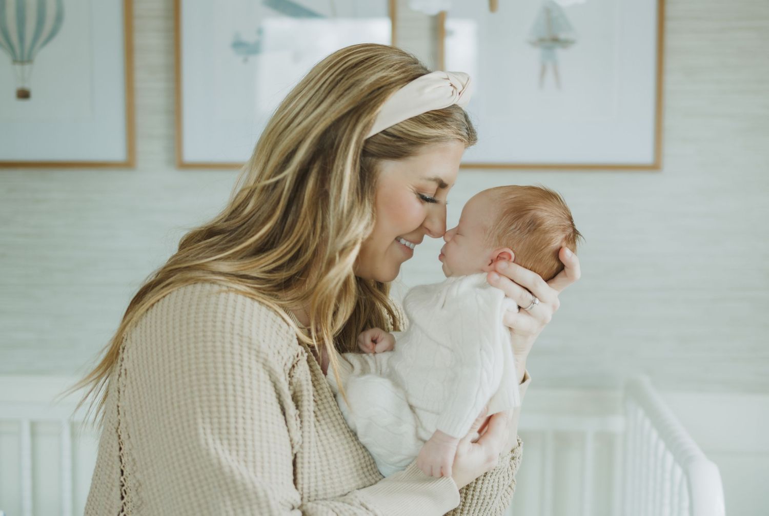 A mother tenderly touches noses with her newborn baby in a softly decorated nursery room.