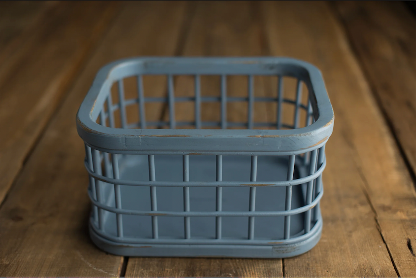 Small gray plastic storage basket with grid pattern sides sitting on rustic wooden surface.