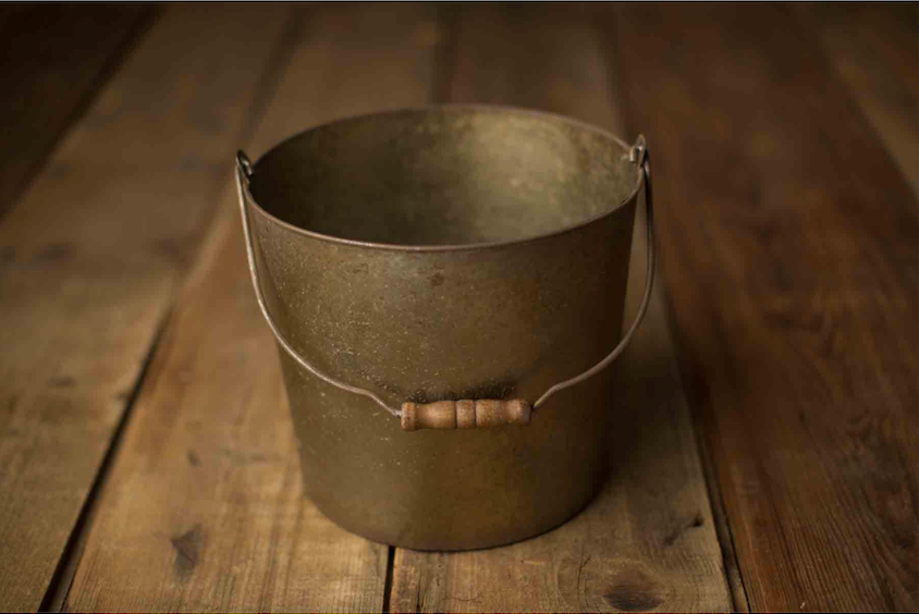 Antique brass bucket with wooden handle sitting on rustic wooden planks background.