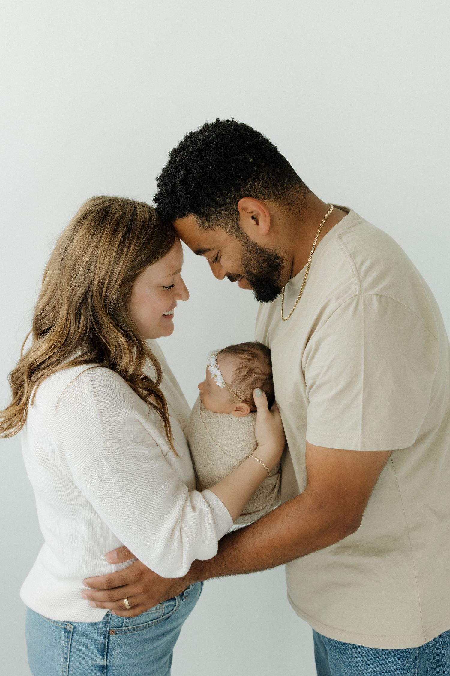 A couple tenderly holds their newborn baby, touching foreheads together in a soft studio portrait.