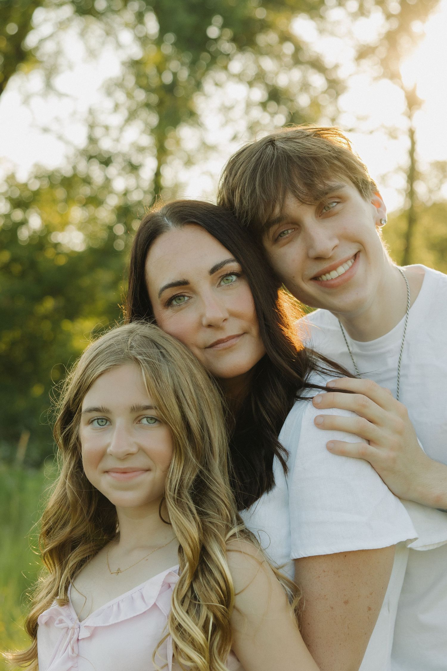 Three friends pose together outdoors during golden hour with natural sunlight creating a warm glow.