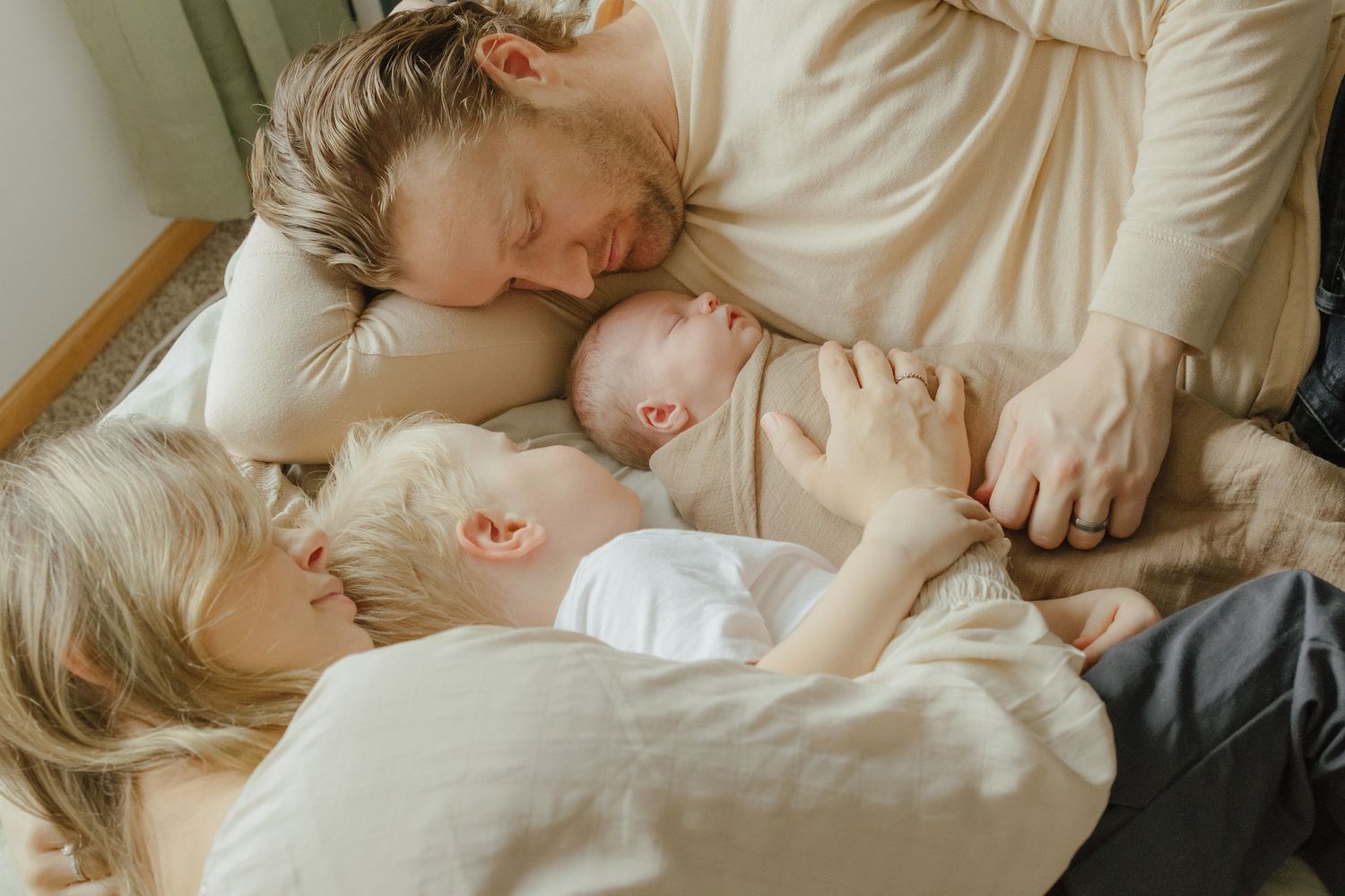 A person and baby sleeping together peacefully on white bedding in soft natural light.