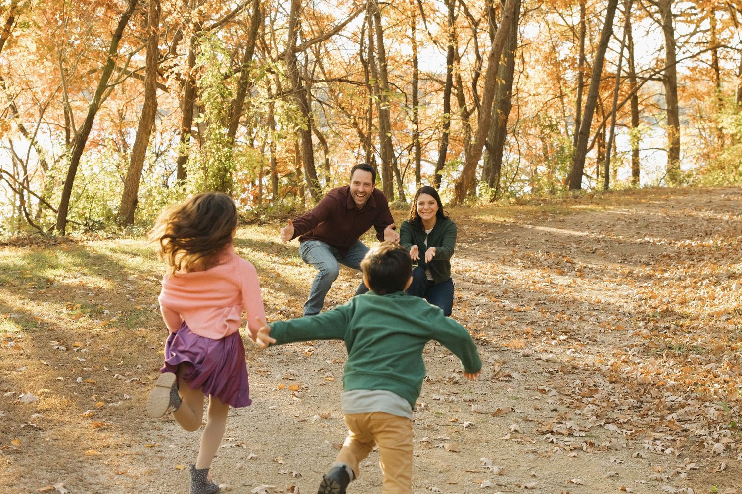 Family running toward each other in an autumn forest with golden leaves, parents welcoming children with open arms.