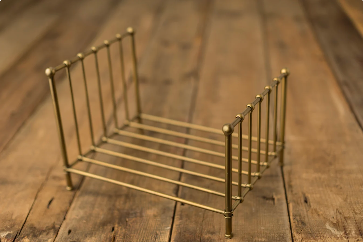 Gold metal miniature bed frame prop on rustic wooden surface, perfect for newborn photography sessions.