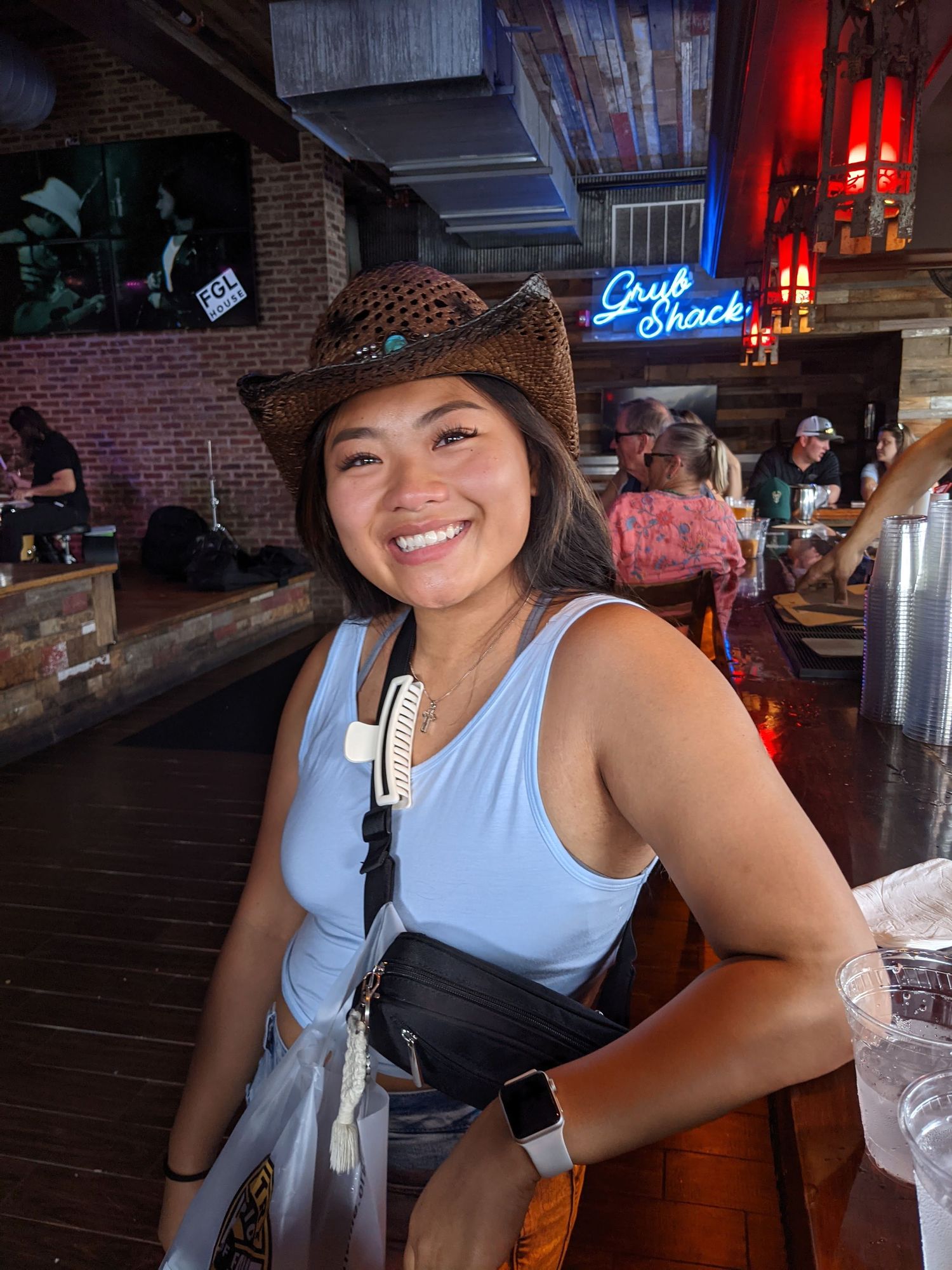 Person in casual summer attire smiling at a bar with dimly lit red lighting in the background.