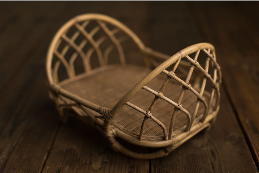 Small wicker rattan basket with lattice weave design and brown cushion on rustic dark wood surface.