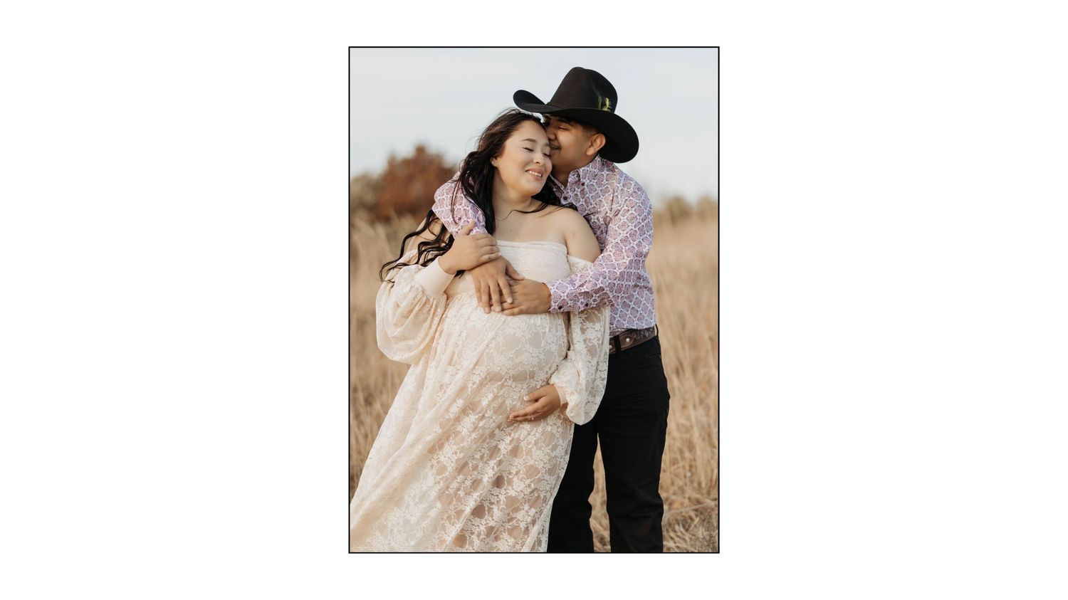 A romantic couple poses together in a sunny field wearing western style clothing.