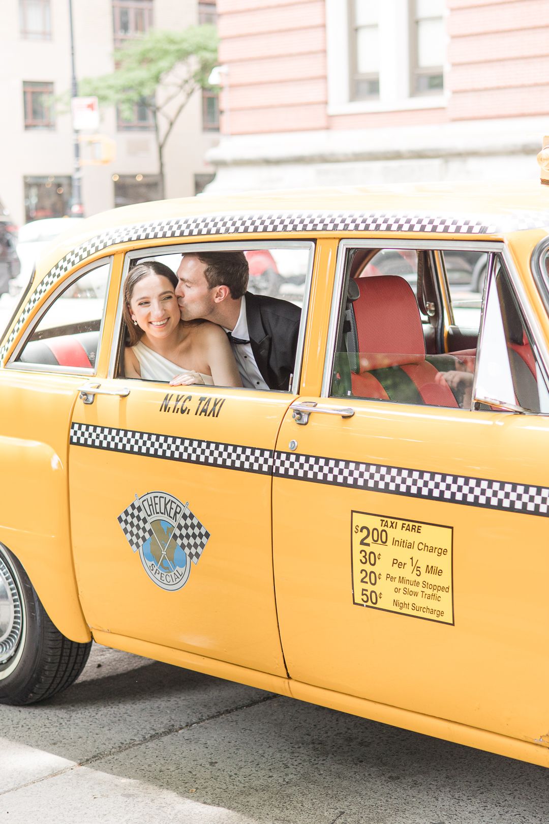 Wedding couple laughing together in the back seat of a vintage yellow New York City taxi.