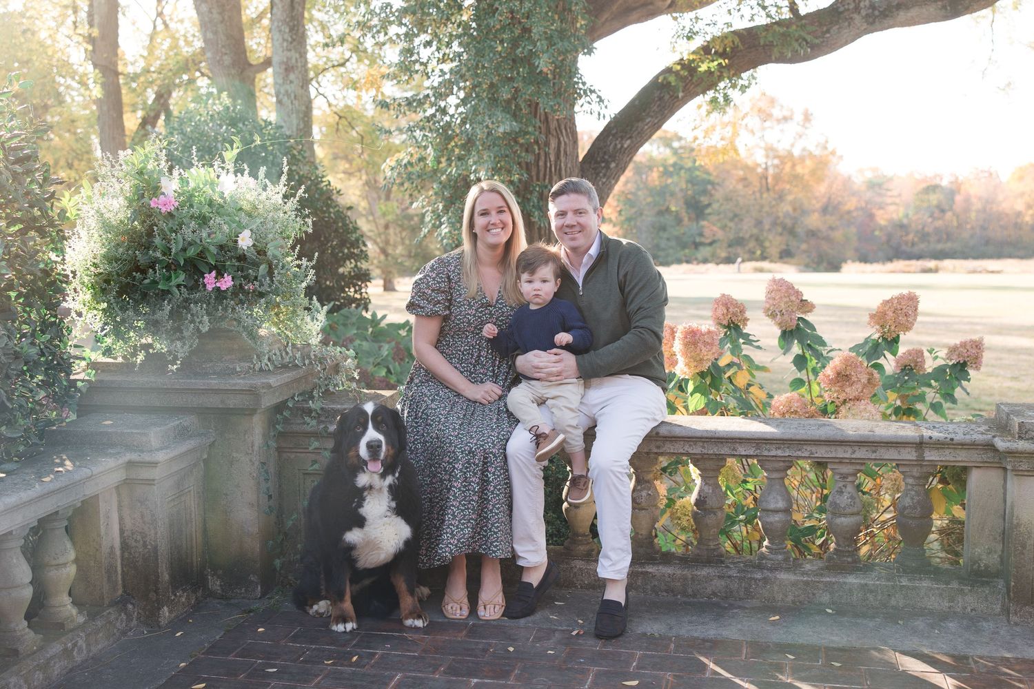 Family portrait with dog sitting on stone balcony during golden hour.