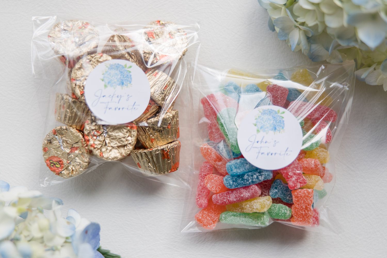 Two clear favor bags filled with colorful candy and cookies with blue monogram stickers.