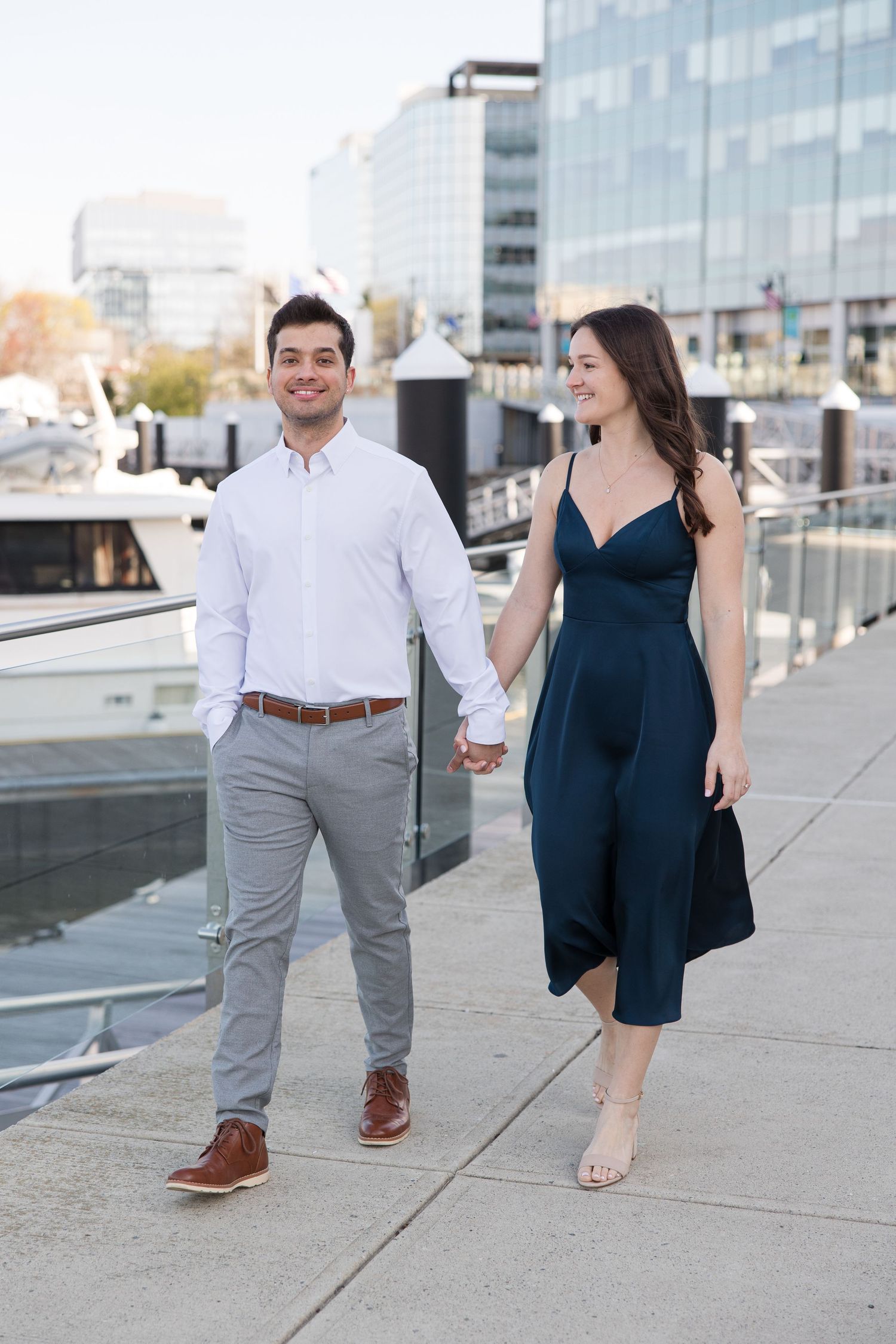 A couple walks together on an urban waterfront boardwalk in formal attire.
