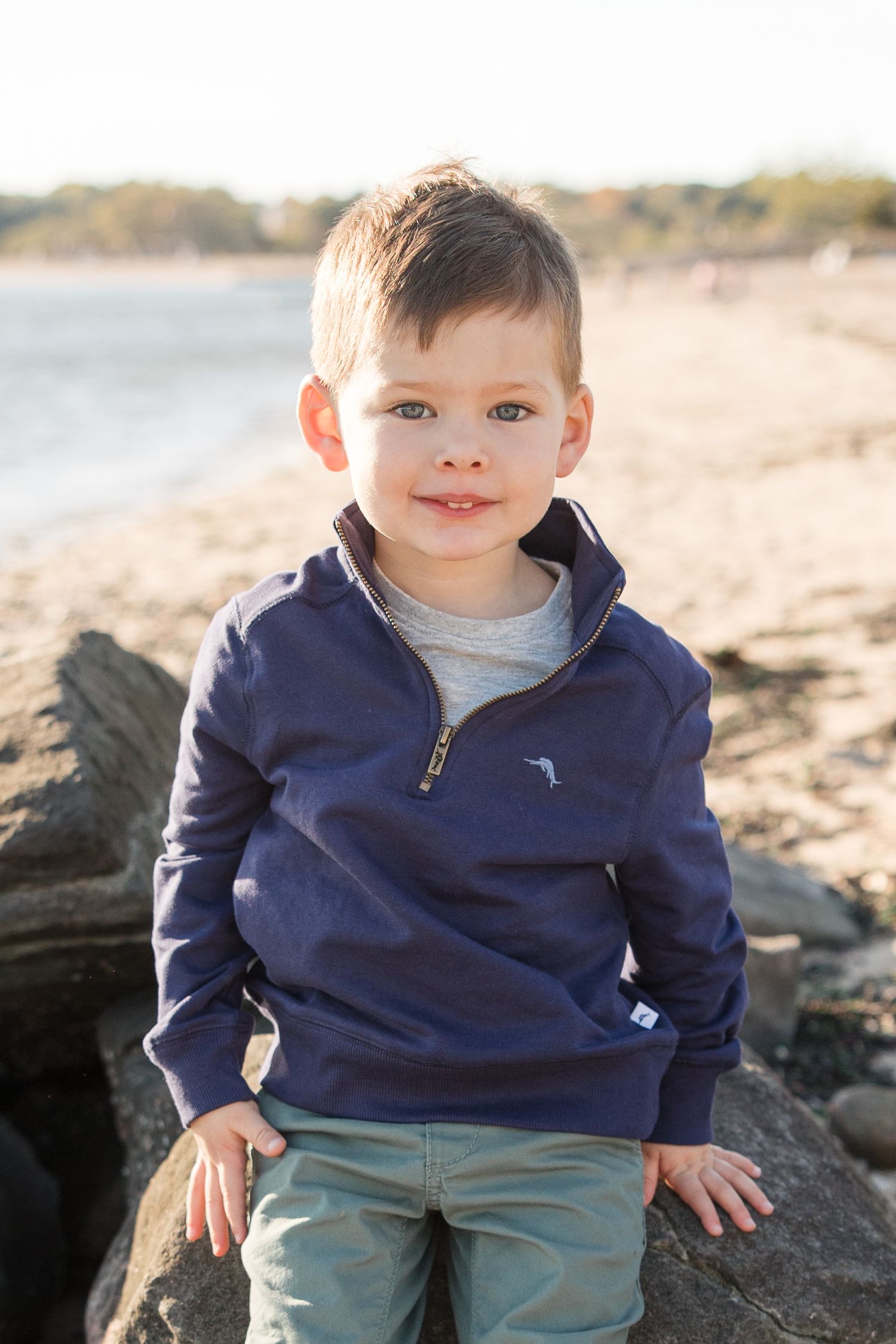 A child sitting on coastal rocks wearing a navy blue pullover.