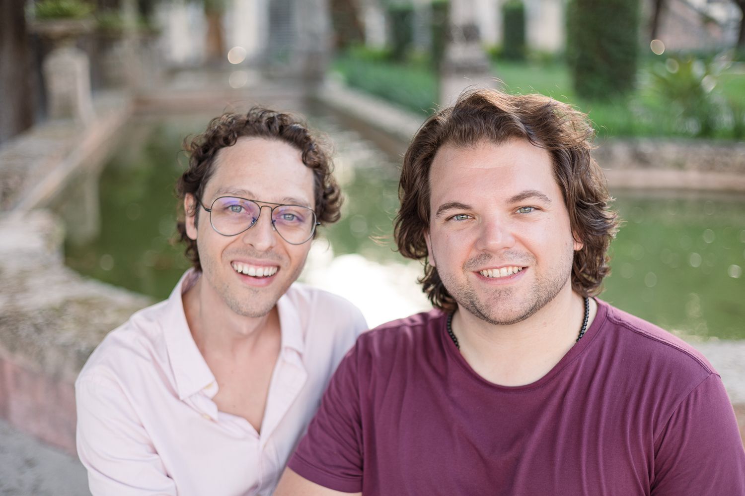 Two people smile brightly at the camera while sitting outdoors.