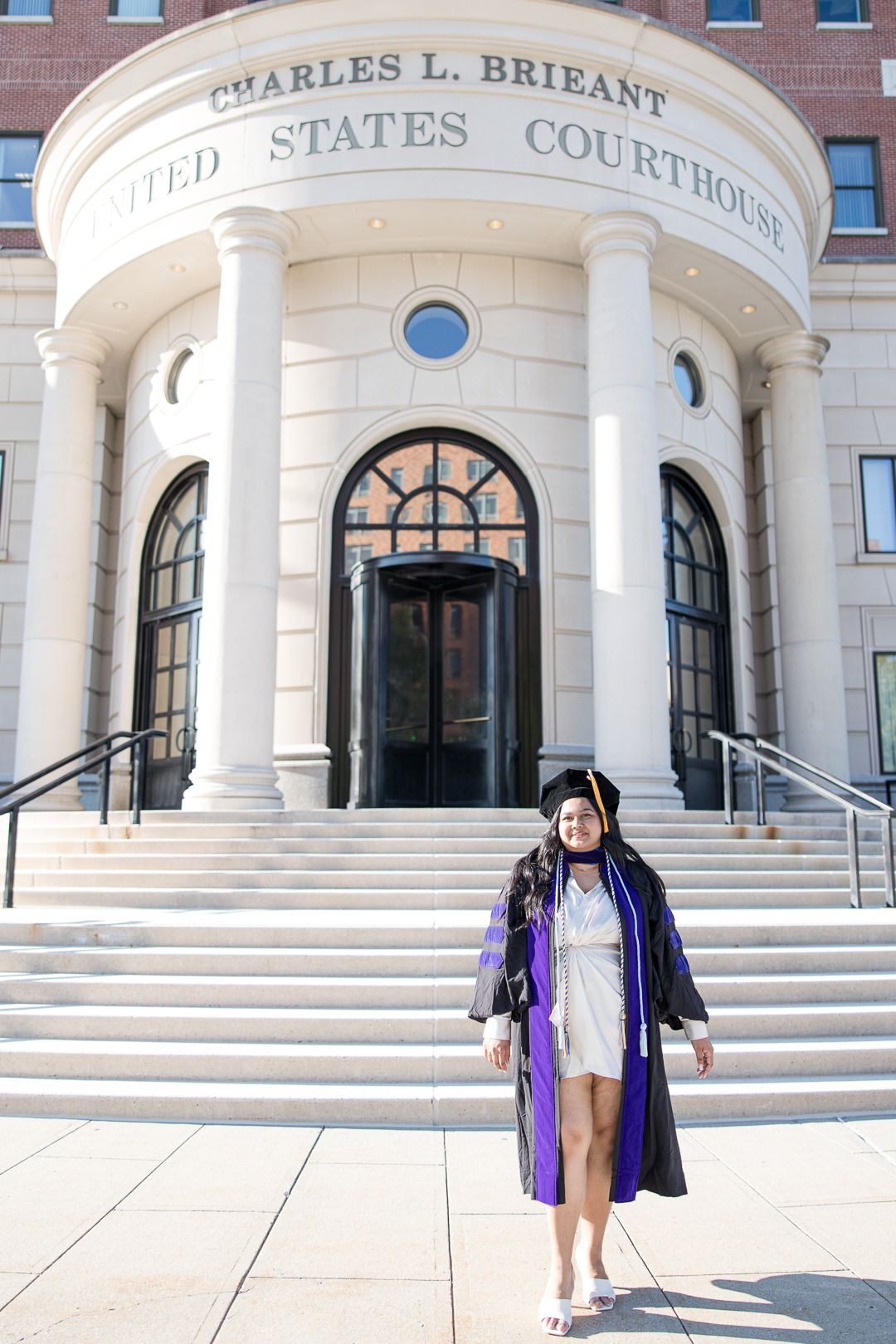 Graduate in purple regalia standing on steps of Charles L. Briant United States Courthouse.