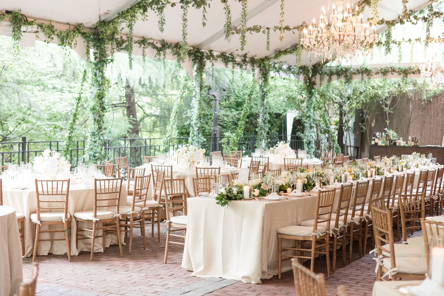Dreamy wedding reception tent decorated with hanging greenery, chandeliers and chiavari chairs.