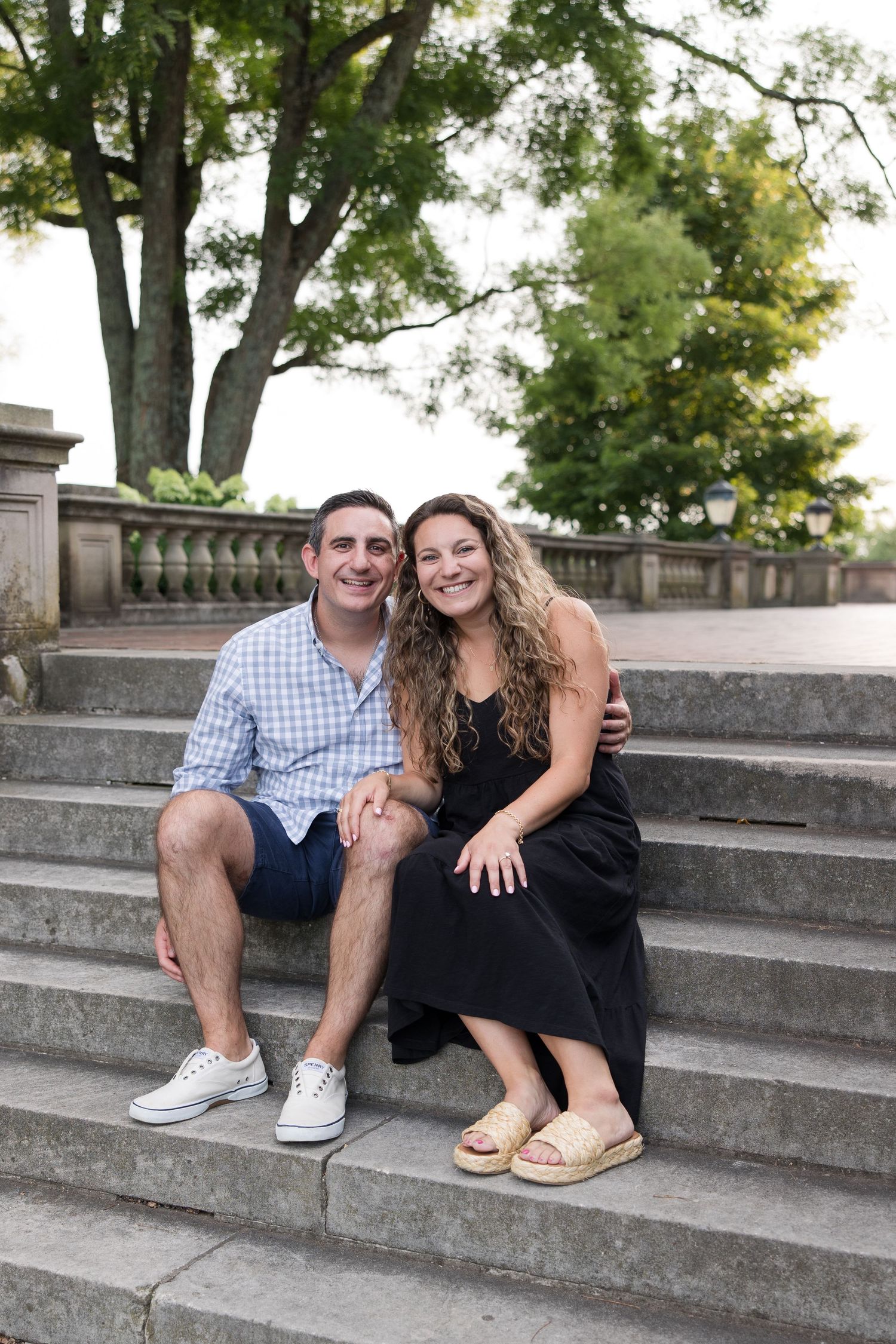 A happy couple sits together on grand stone steps during their engagement photo session.