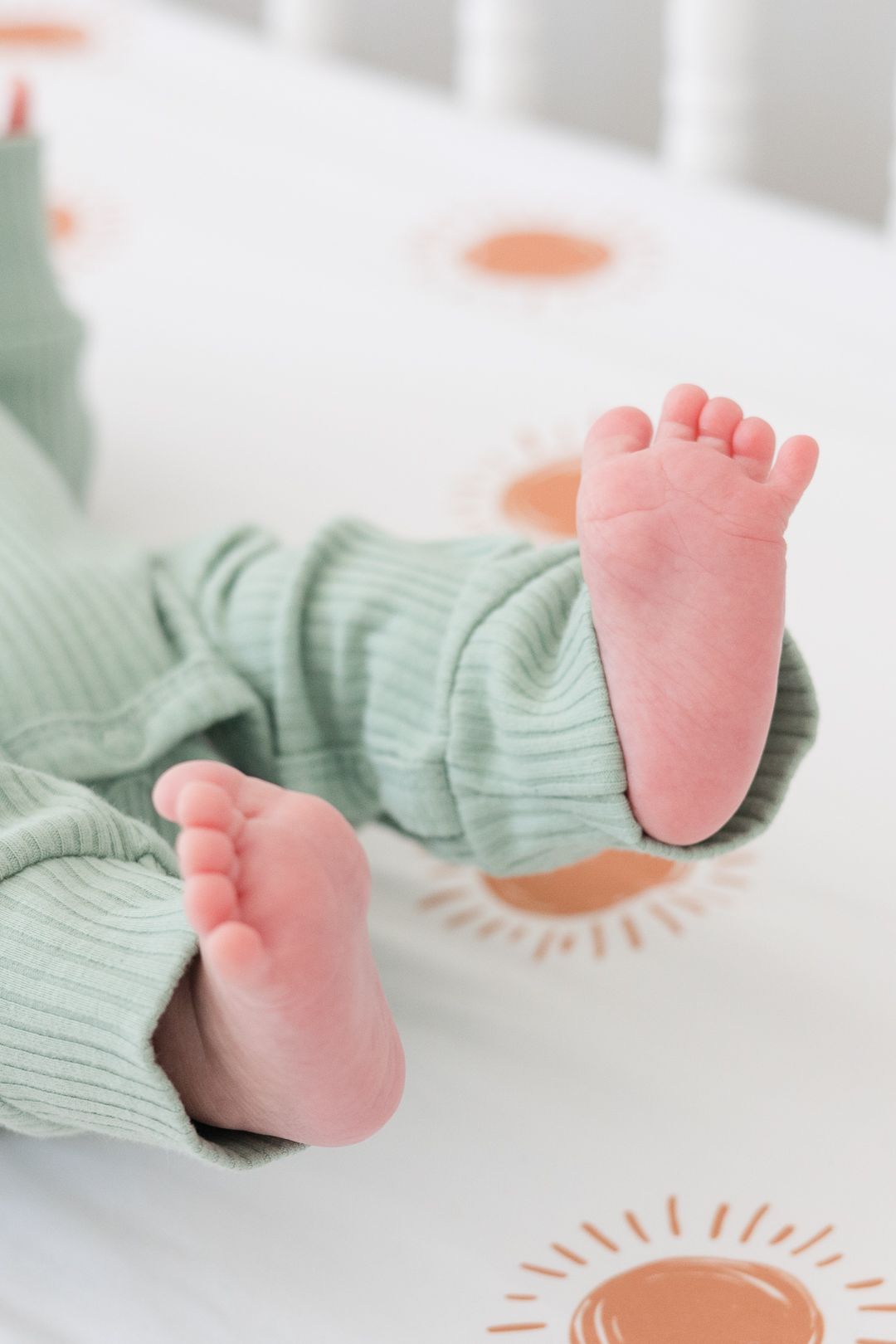 Tiny pink newborn baby feet peek out from mint green ribbed clothing against a patterned sheet.
