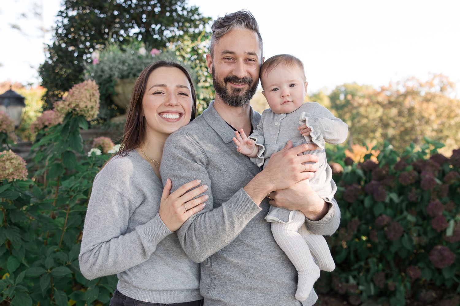 Family wearing coordinating grey outfits pose together in garden setting.