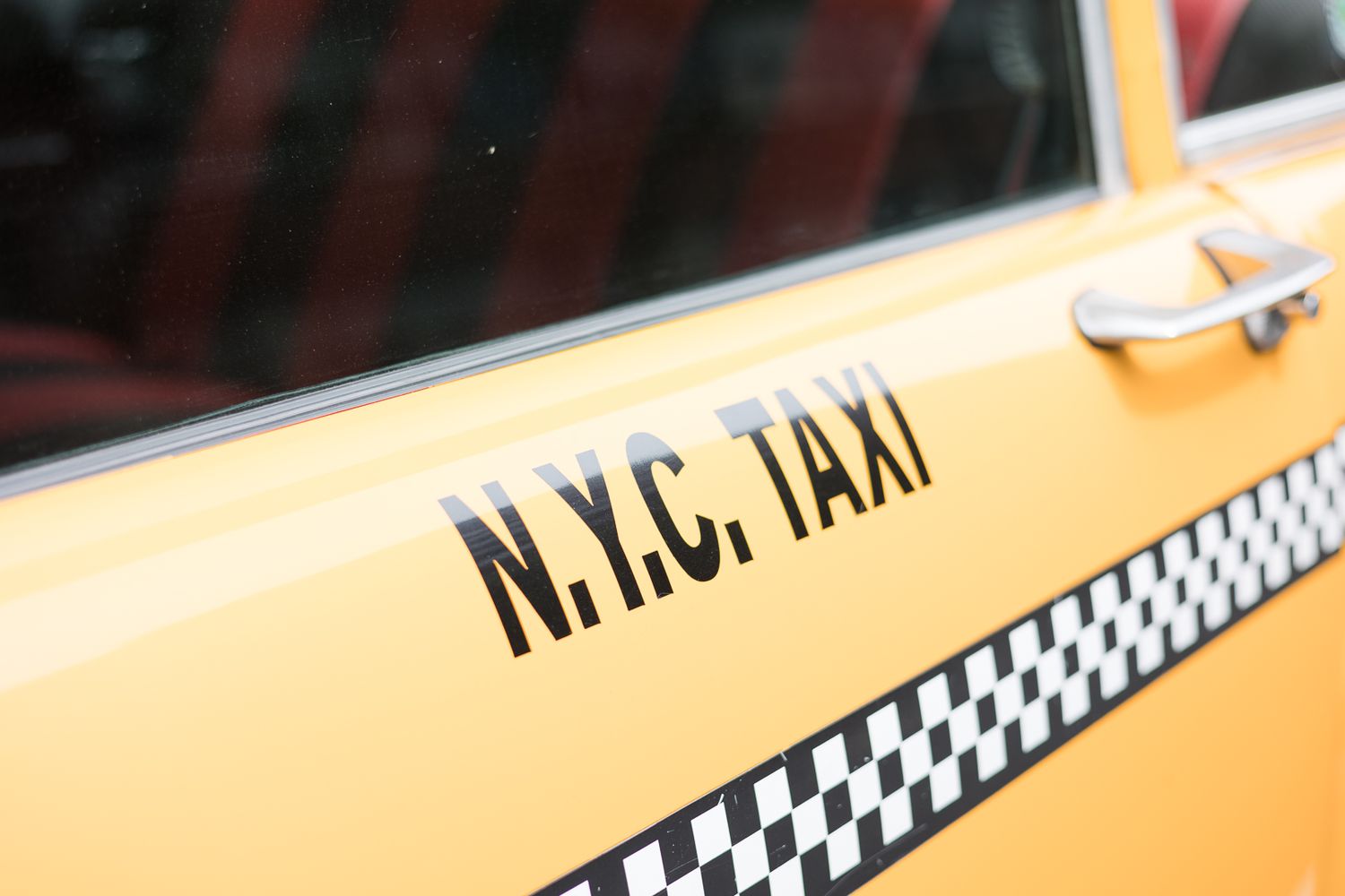 Close-up detail shot of N.Y.C. TAXI lettering on a yellow cab door with checkered stripe.