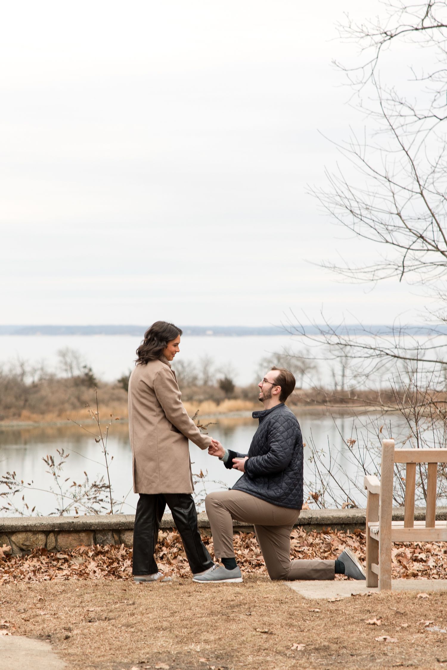 A marriage proposal moment captured by a lake with autumn leaves on the ground.
