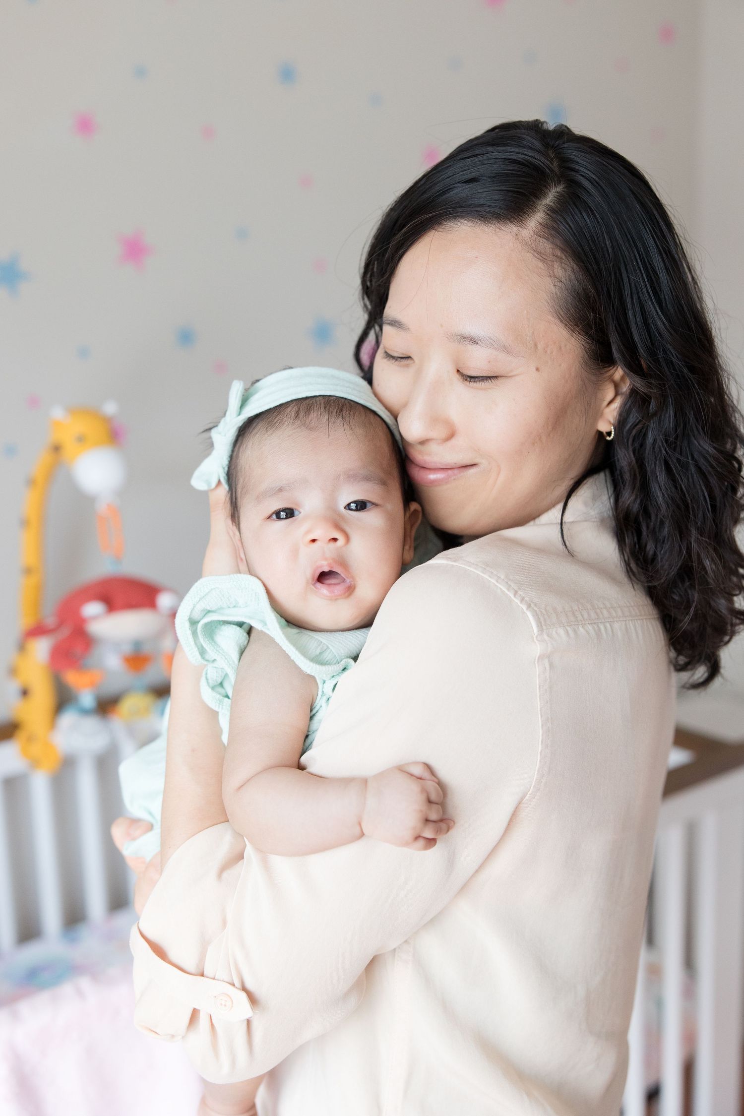 Tender nursery moment with soft polka dot background and baby toys visible.