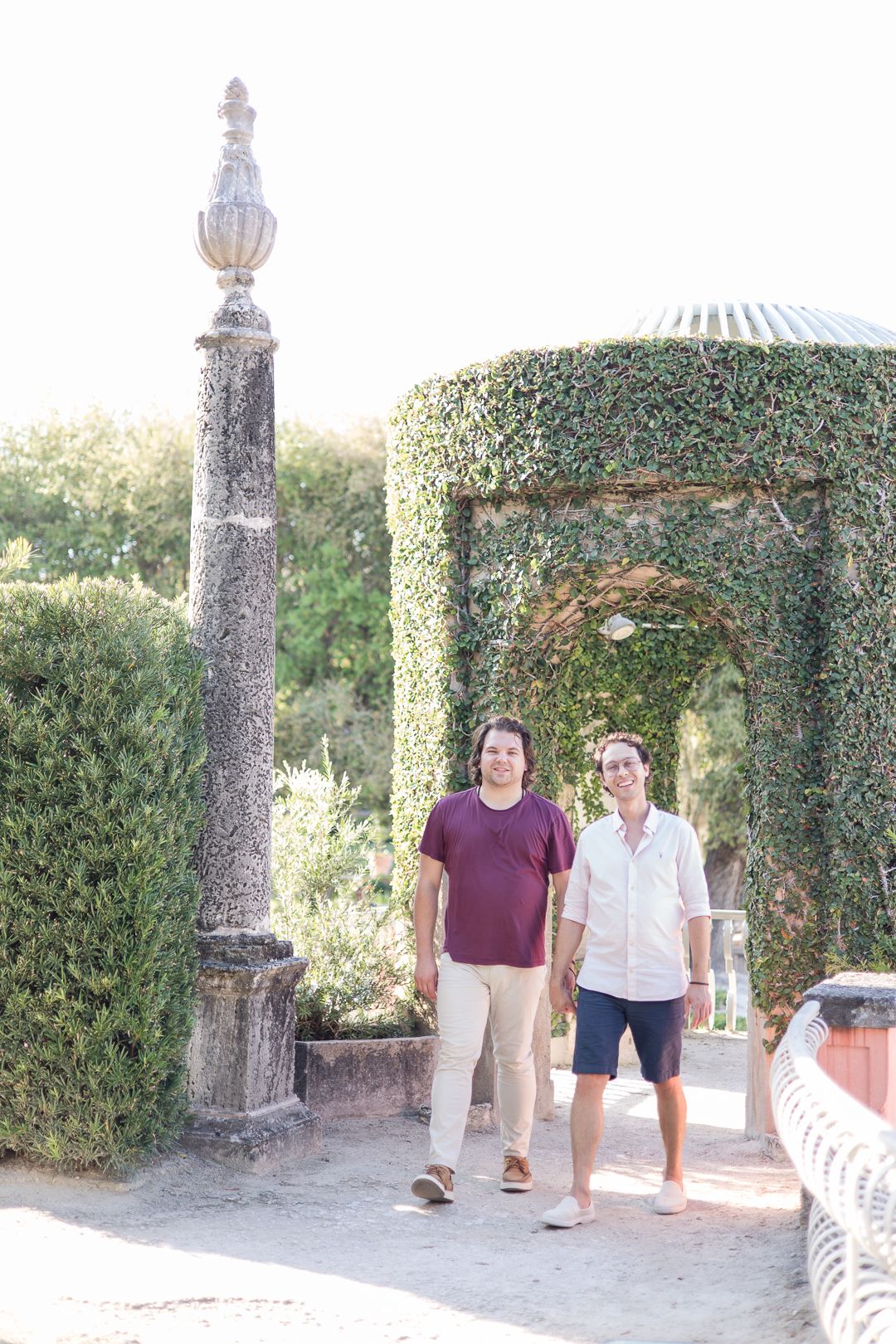 Garden scene with ornate stone pillar and vine-covered gazebo.