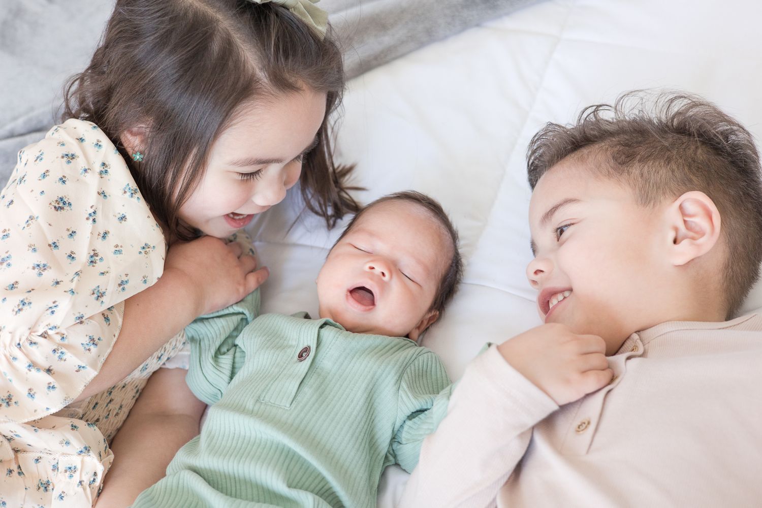 Three siblings share an intimate moment laying together on white bedding.