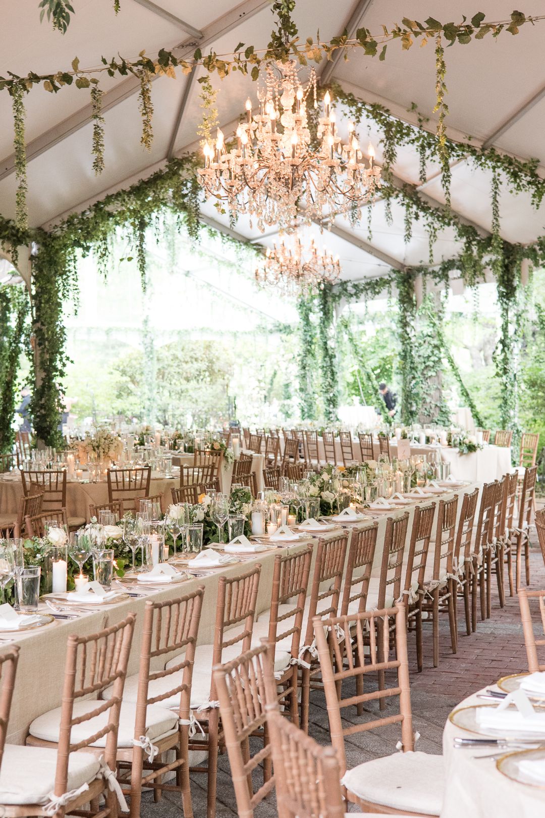 Crystal chandeliers and cascading greenery adorn an elegant wedding reception tent.
