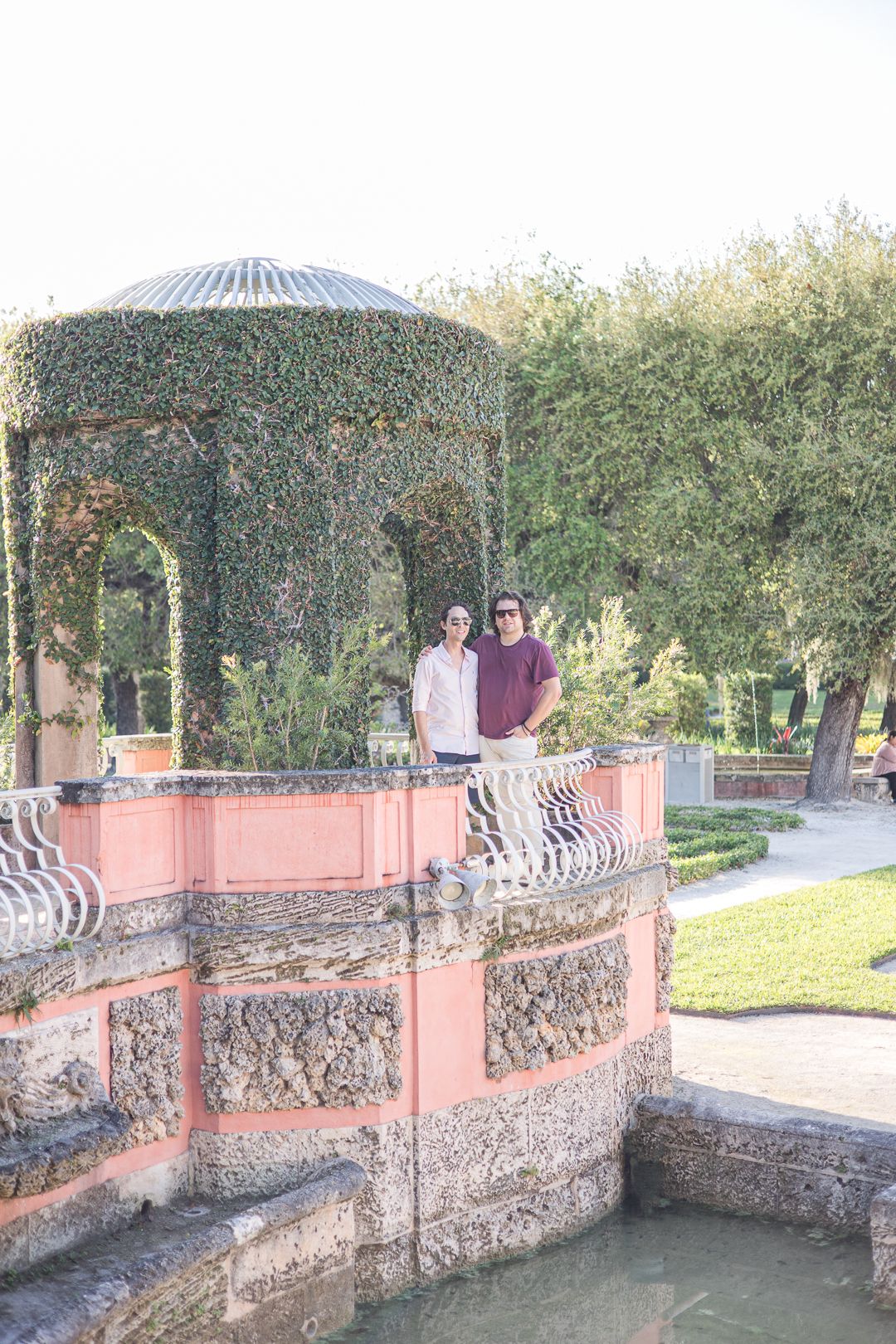 Two people standing in a decorative gazebo overlooking landscaped gardens.