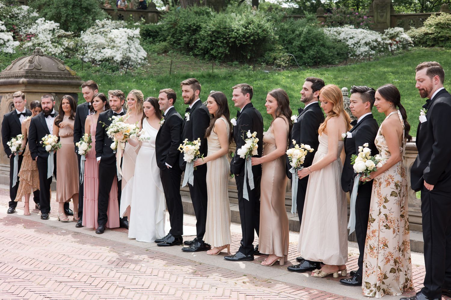 Wedding party lined up on brick pathway with bridesmaids in neutral tones and floral dresses.