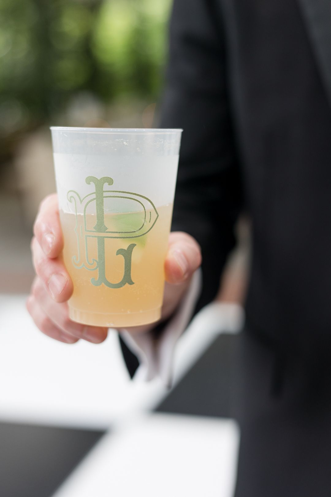 Hand holding a frosted cocktail glass with decorative monogram design.