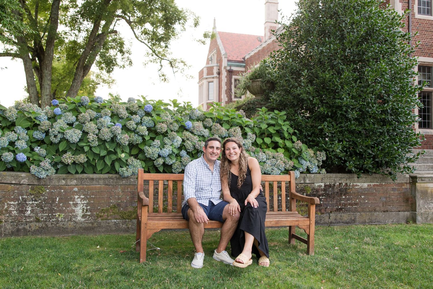 A wooden bench sits in a garden setting with hydrangea bushes and architectural details in the background.