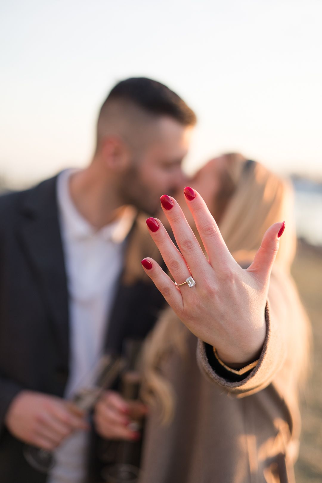 A close-up of a hand showing off an engagement ring with red nail polish.