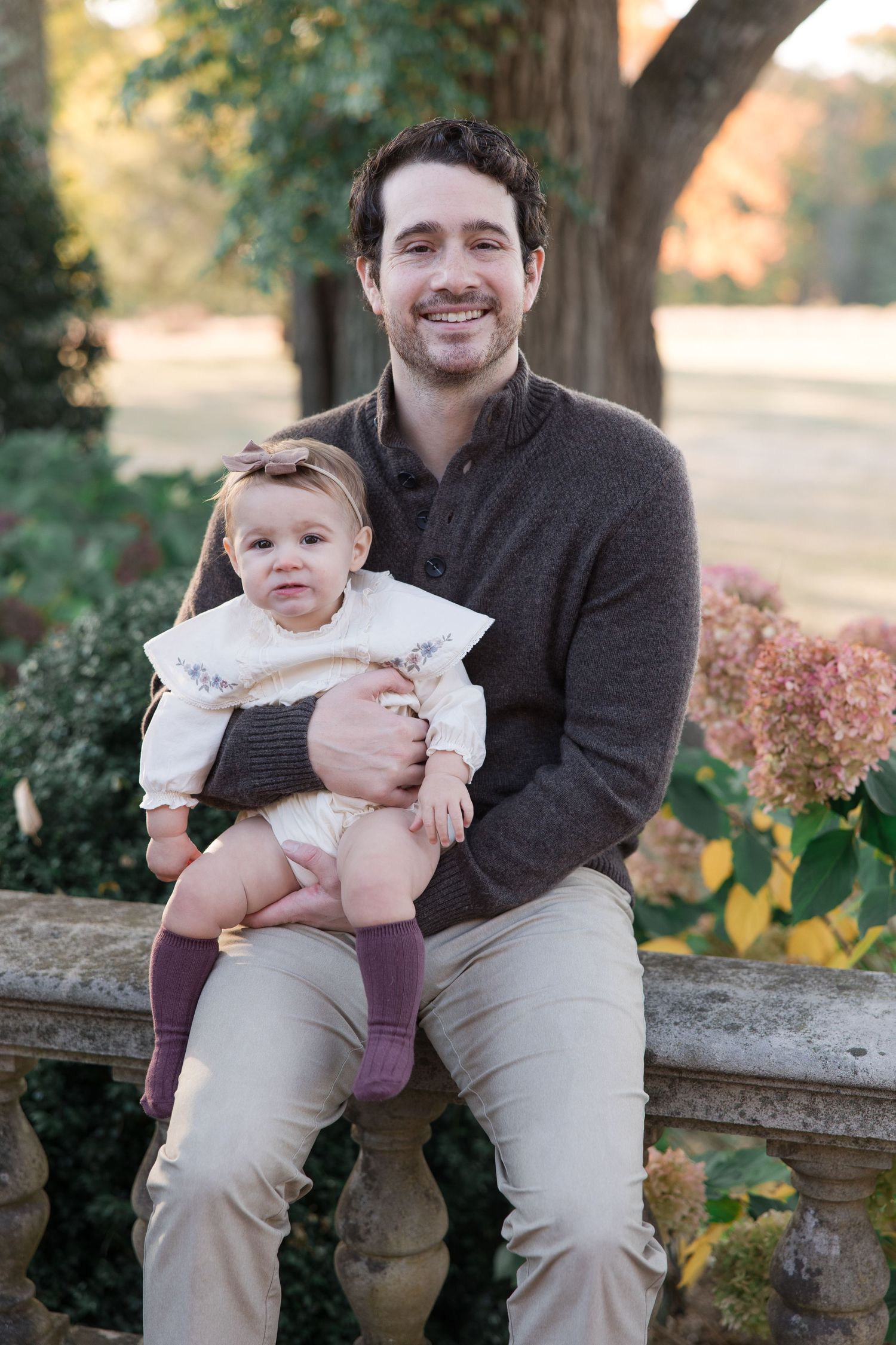 Parent and baby portrait on stone bench in autumn garden setting.