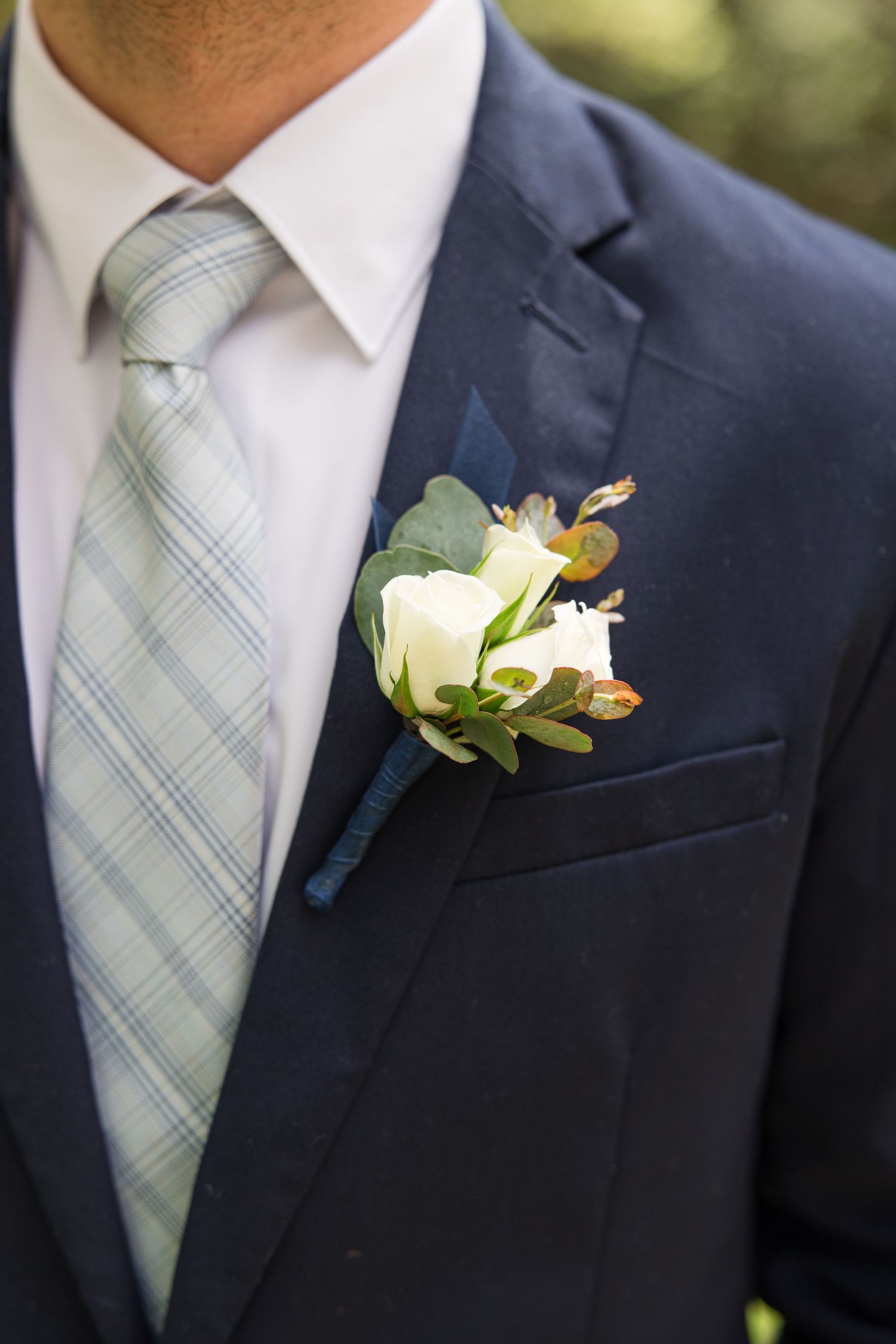 Close-up of groom's navy suit with plaid tie and white rose boutonniere.