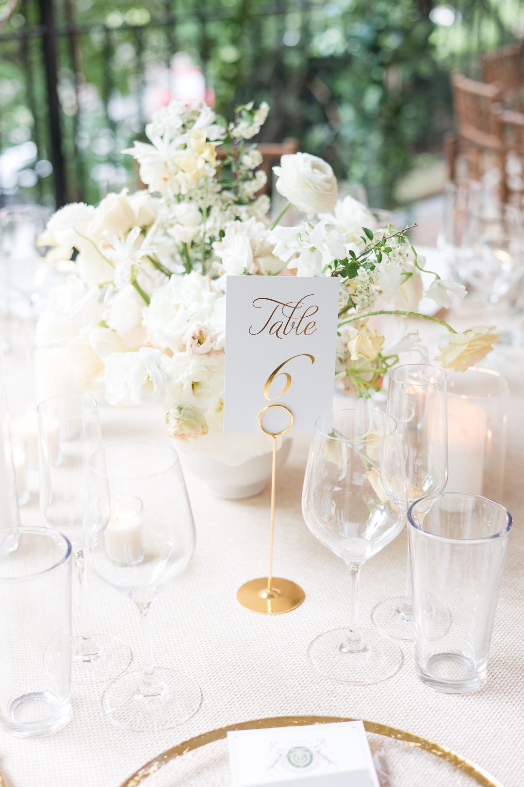Elegant table setting with white flowers, gold-rimmed table number, and crystal glassware.