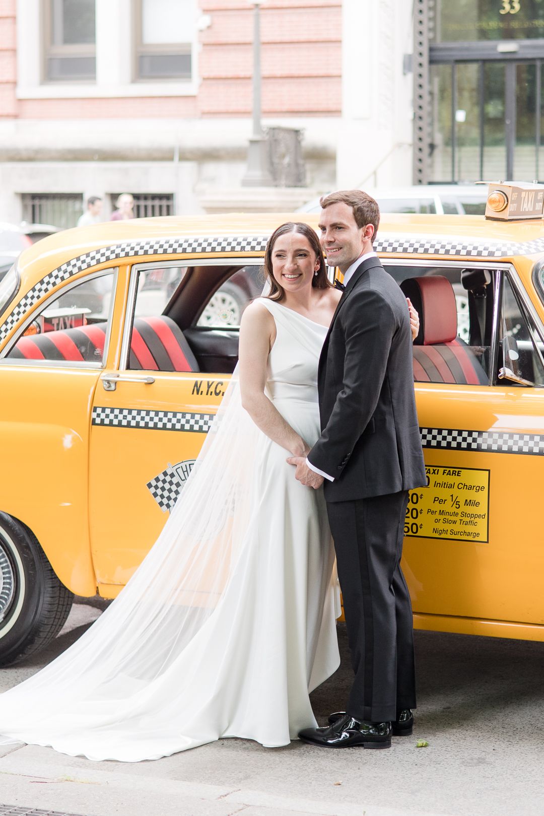 A wedding couple stands beside a vintage yellow taxi in an elegant urban photo shoot.