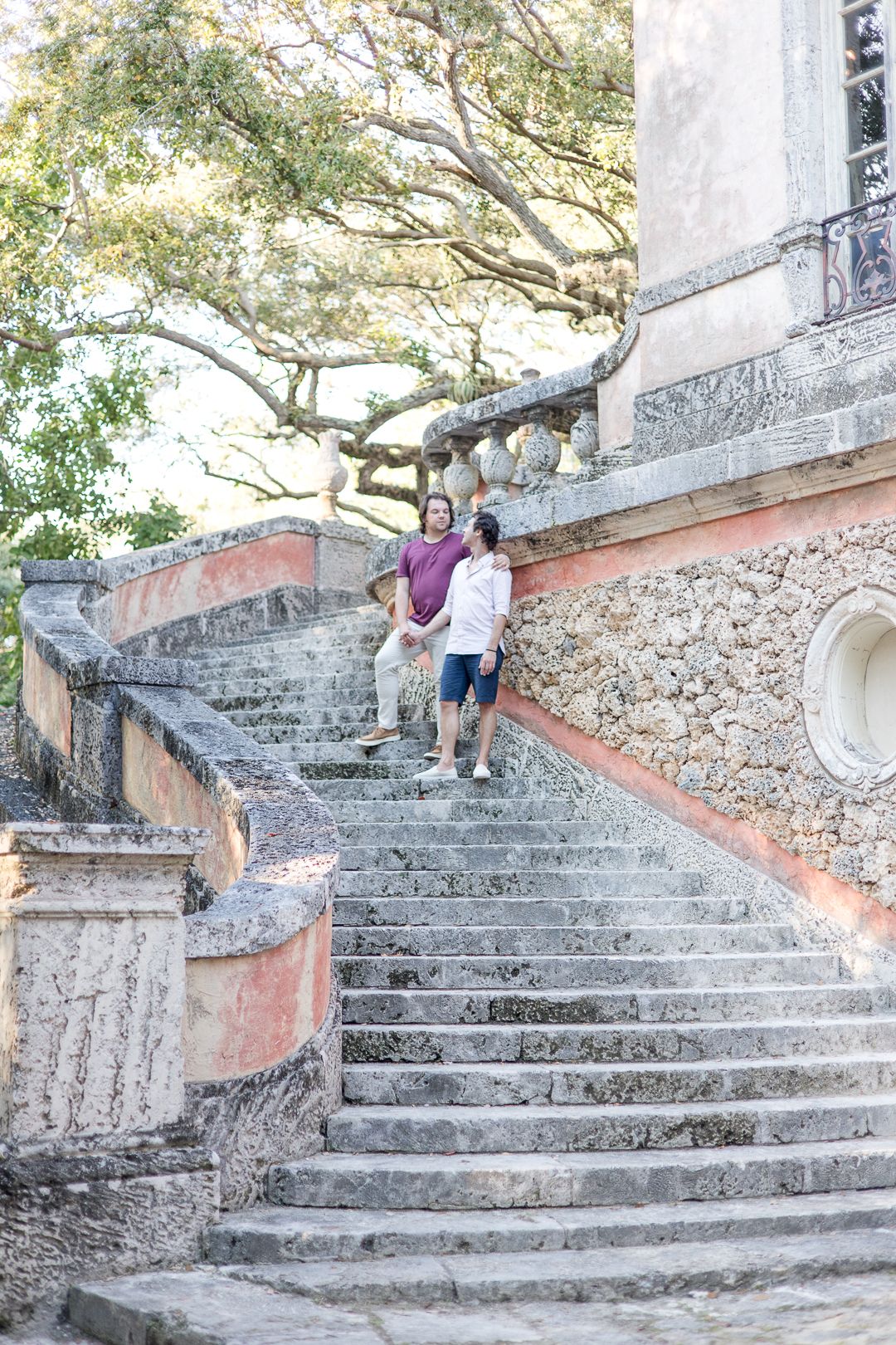 Two people ascending grand stone steps of a historic building surrounded by trees.