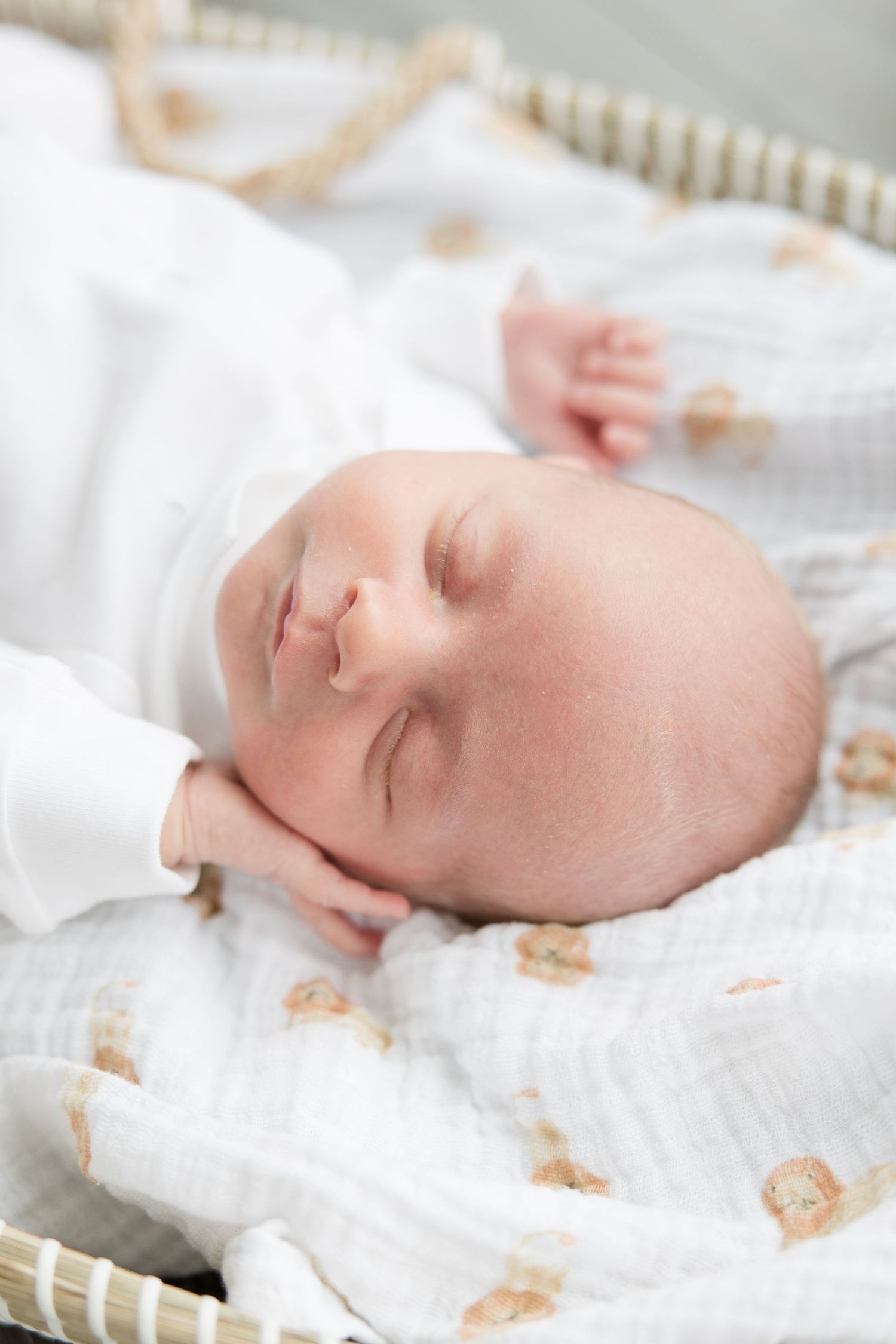 A peaceful sleeping baby rests on white bedding with a soft decorative pattern.