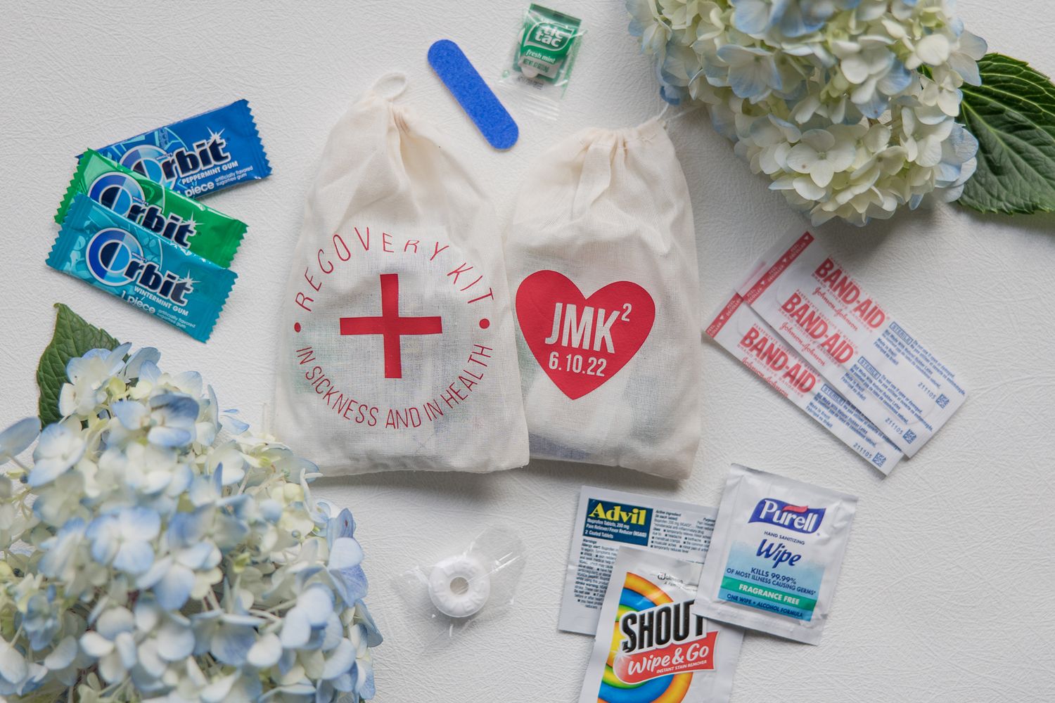 Wedding welcome bag items including first aid kits, gum, and hand sanitizer arranged with blue hydrangeas.