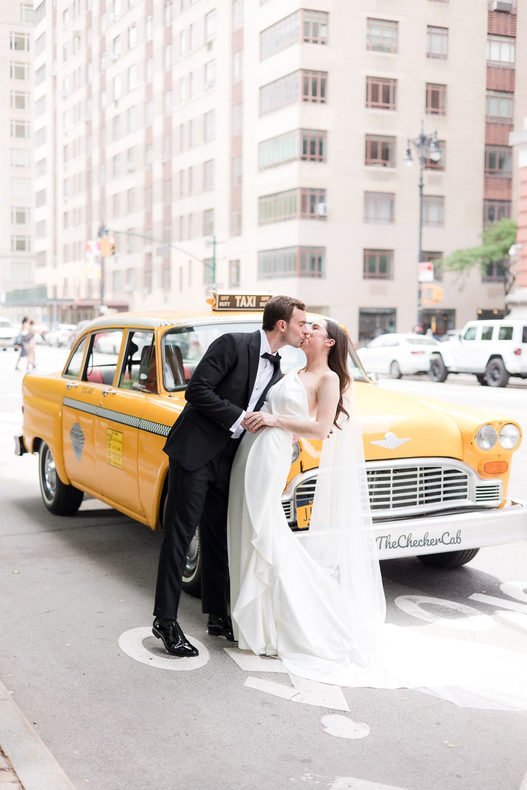 A dreamy wedding portrait with a couple leaning against a yellow taxi on a city street.