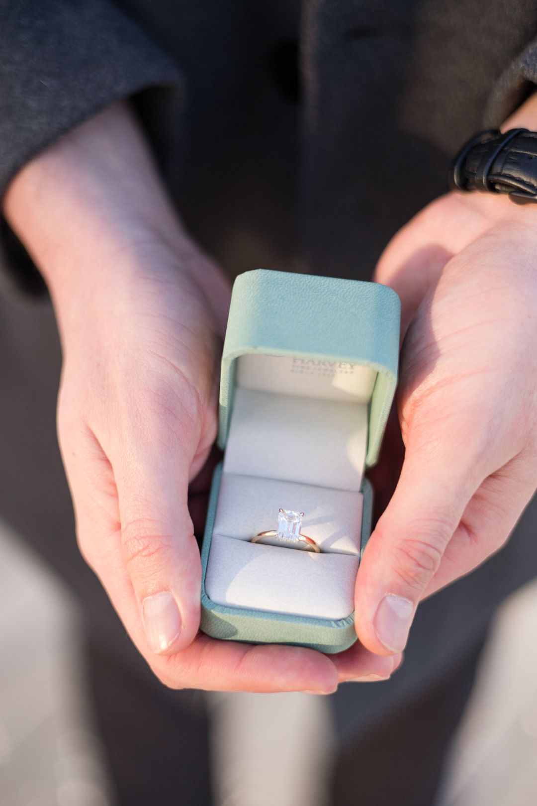 An engagement ring in a light blue box held in hands.