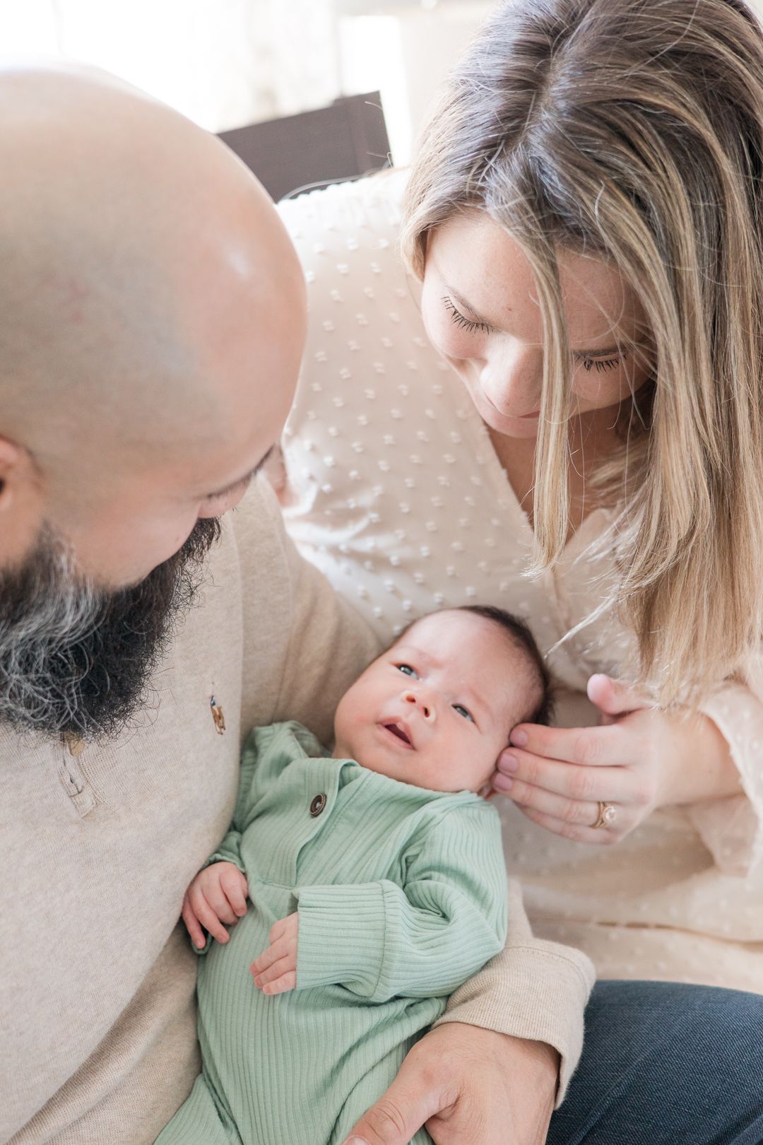Parents lovingly gaze at baby wearing mint green outfit during intimate moment.