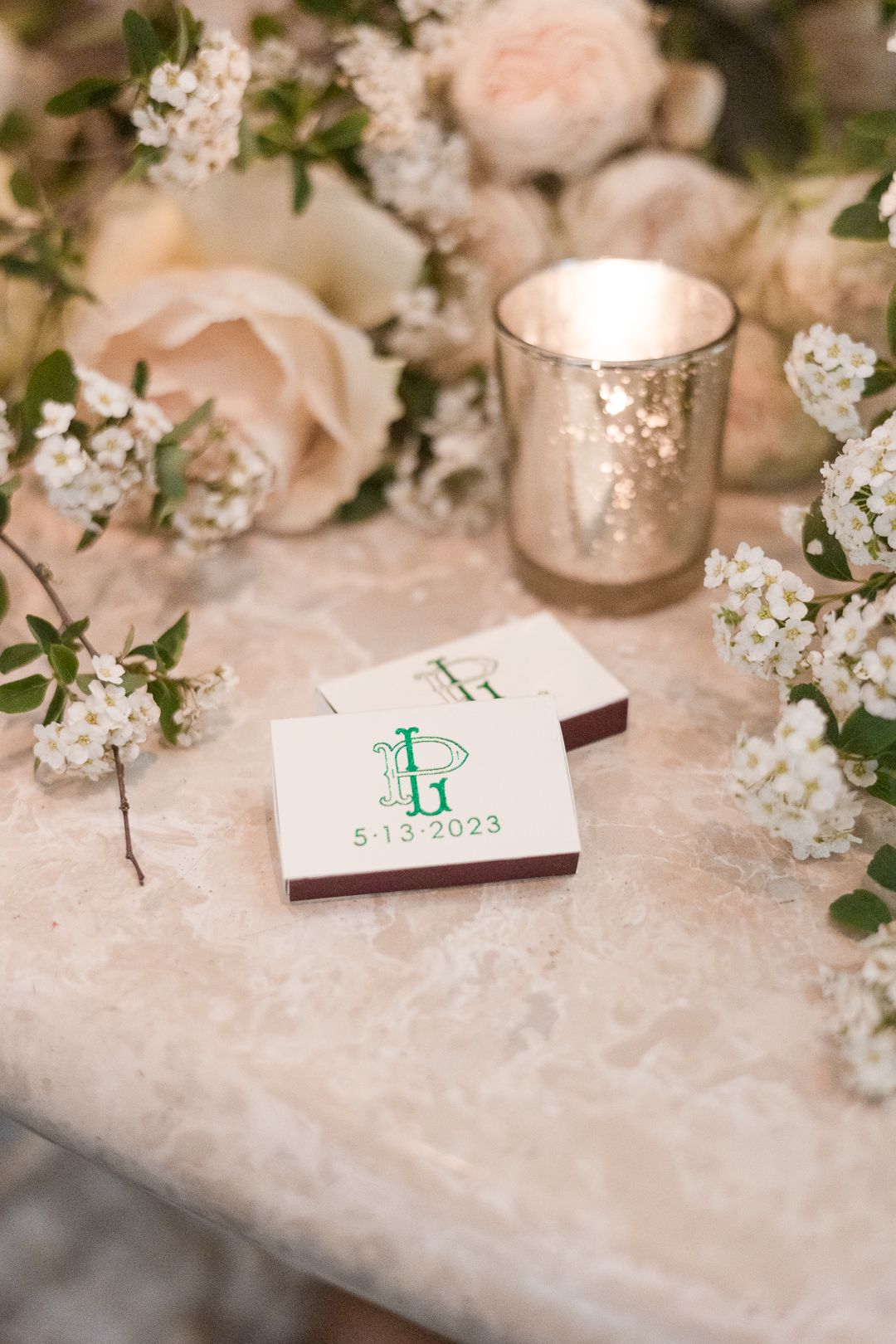 Wedding details featuring blush roses, baby's breath, and a monogrammed card with green lettering.