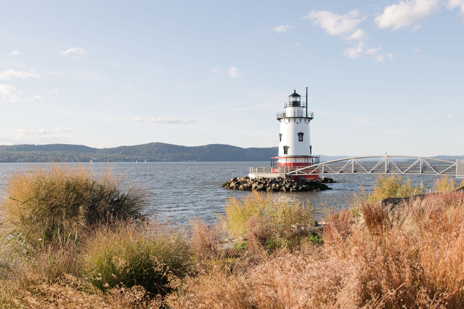 Scenic lighthouse on rocky pier with autumn foliage and calm waters.