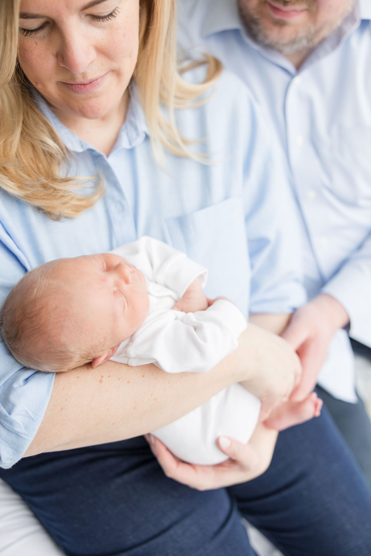 A newborn baby wrapped in white sleeps peacefully while being cradled in a light blue setting.