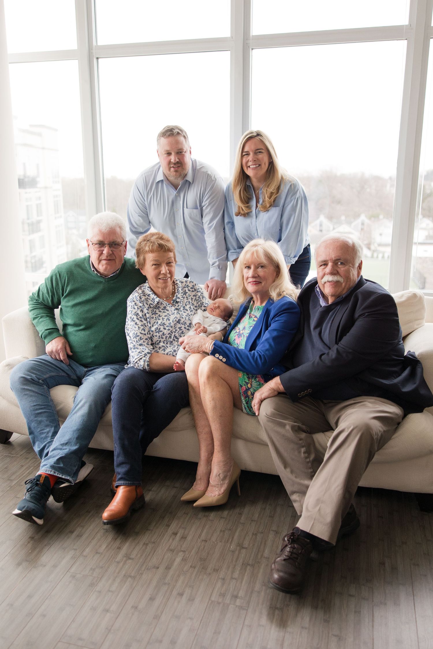 Multigenerational family gathering in bright living room with large windows and modern gray sofa.