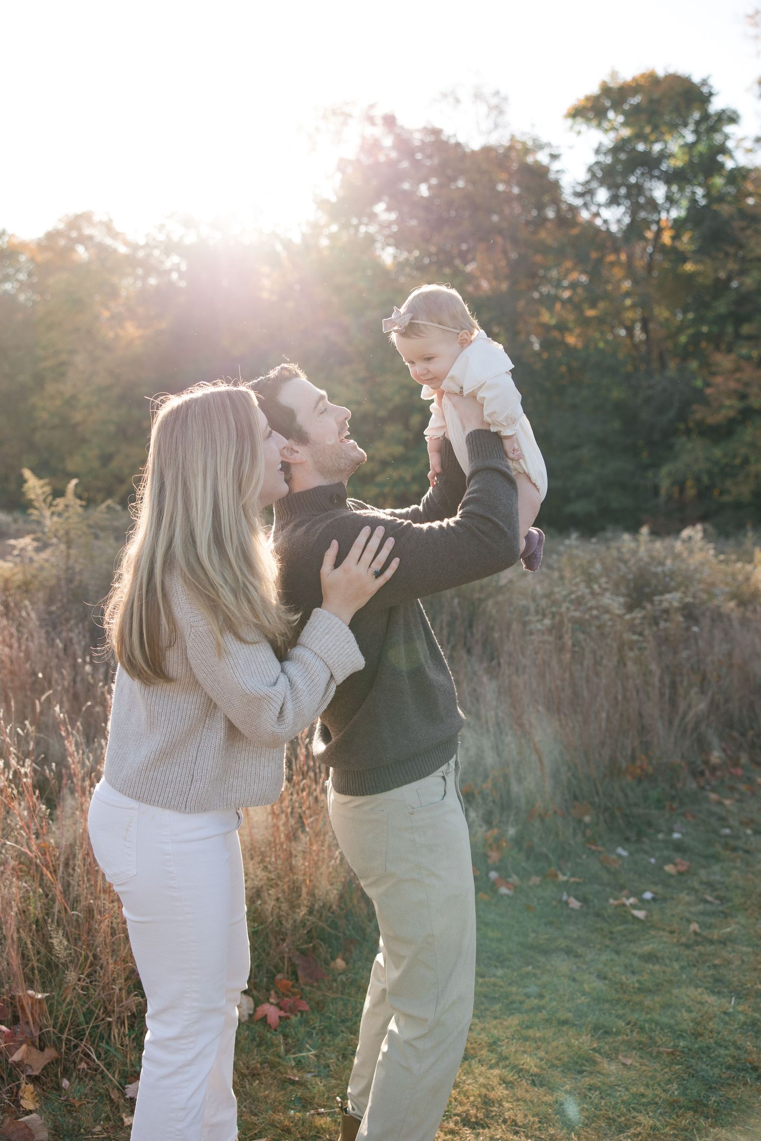 Joyful outdoor family moment with baby being lifted in golden sunlight.