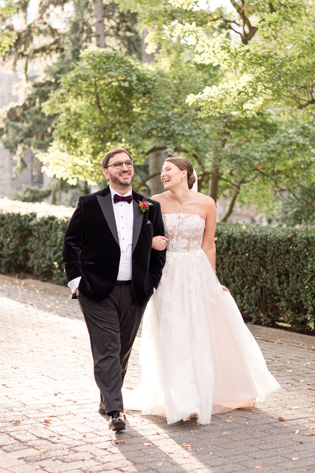 A couple walks together on a stone path surrounded by lush greenery on their wedding day.